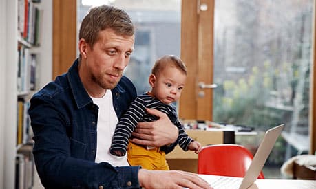A dad working from home on his laptop holding his child