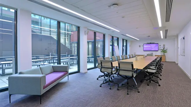 G18 at Alliance Manchester Business School, a modern meeting room with a long conference table, office chairs, large floor-to-ceiling windows, and a seating area.