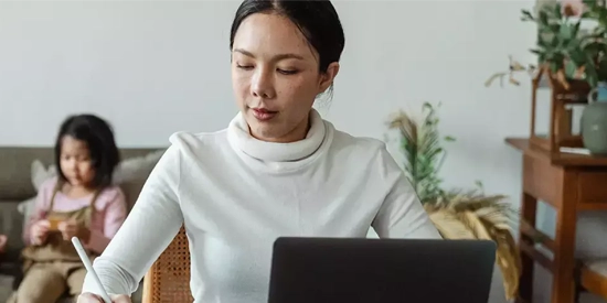 A woman working at a desk with her child sat behind her