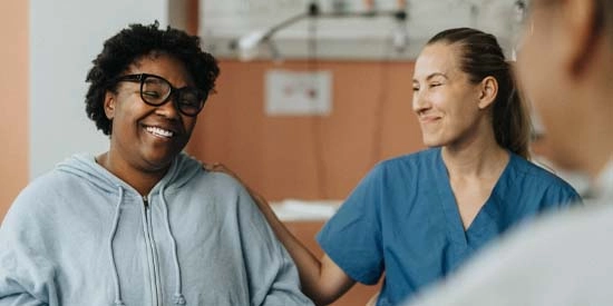 Smiling female nurse consoling happy patient sitting with doctor during a consultation