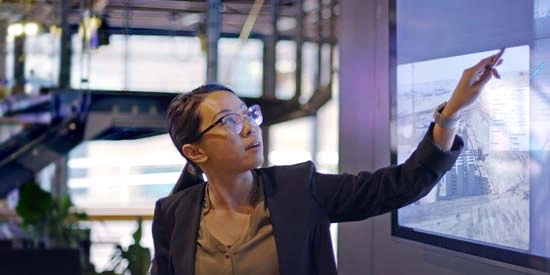 A young Asian woman researcher pointing a large screen that shows data about low carbon electricity production
