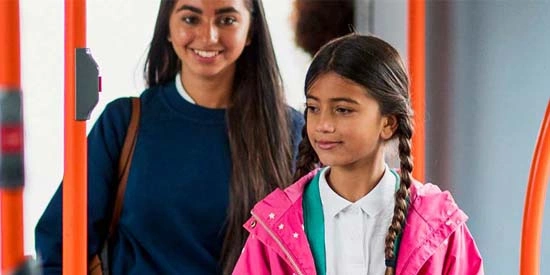 Two young school girls standing up on a bus