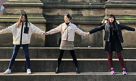 Amanda Kusmajaya holds hands with two friends in front of a statue