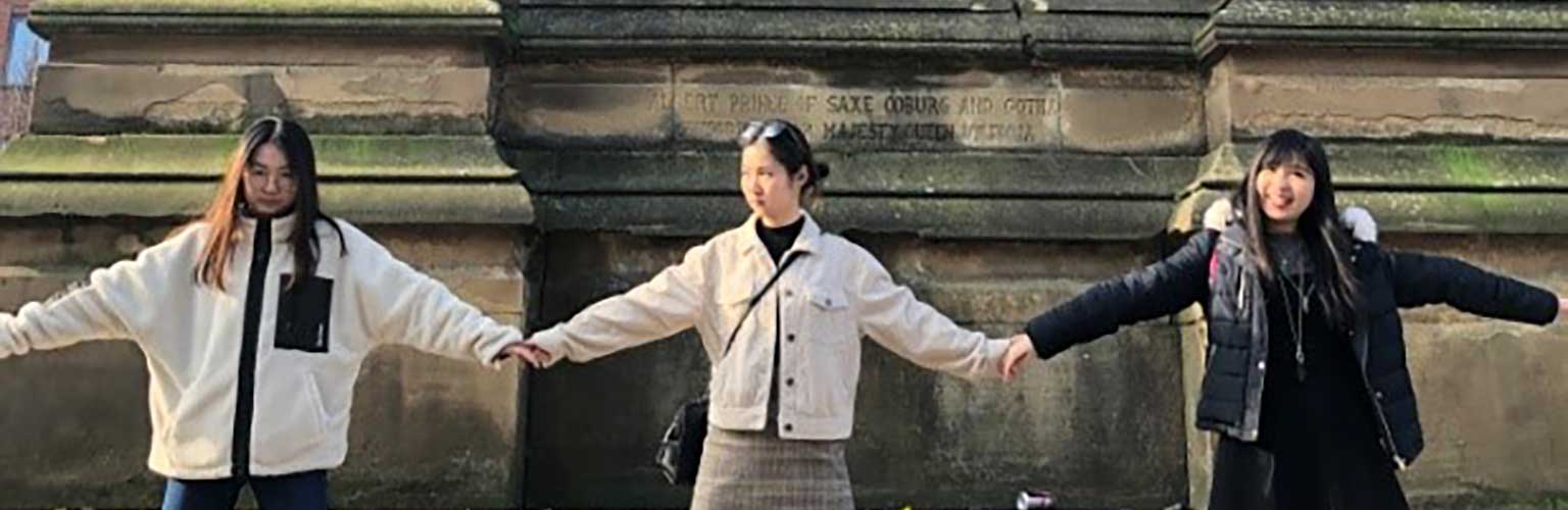 Amanda Kusmajaya holds hands with two friends in front of a statue