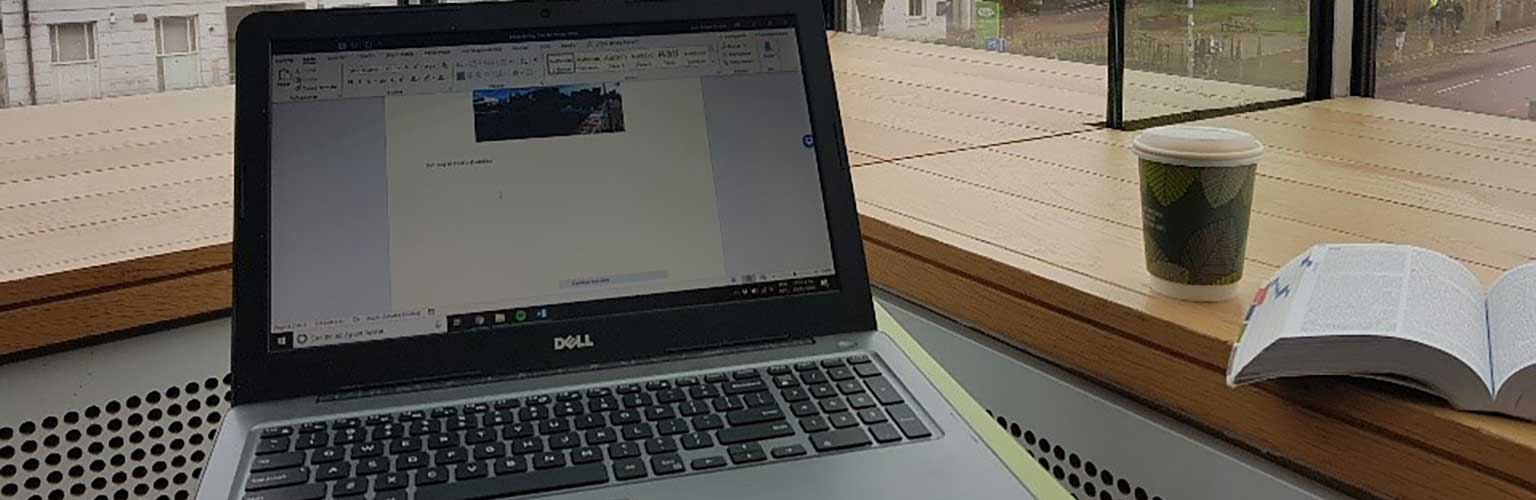 A view of an open laptop in the Learning Commons looking out on Oxford Road, Manchester