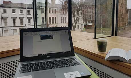 A view of an open laptop in the Learning Commons looking out on Oxford Road, Manchester