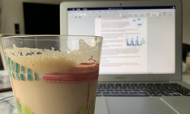 Coffee in the foreground with a document on a laptop in the background
