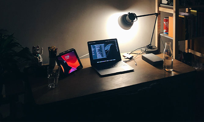 A desk with a laptop on which has been illuminated by a desk lamp