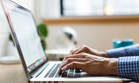 A man typing on a laptop with a blue shirt