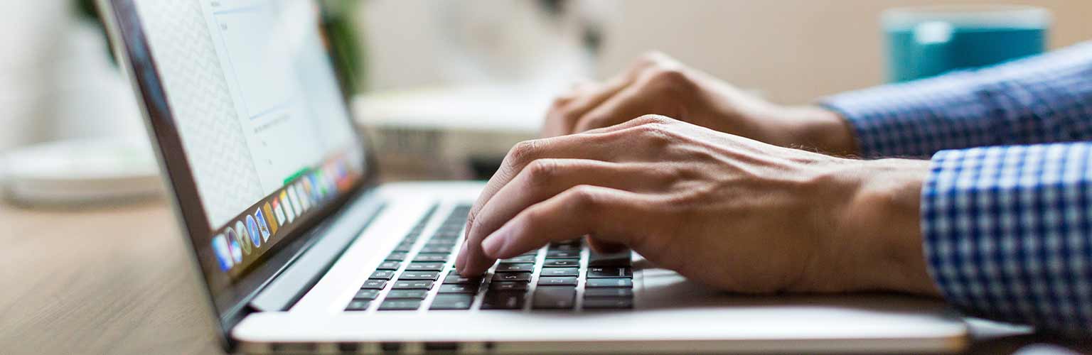 A man typing on a laptop with a blue shirt