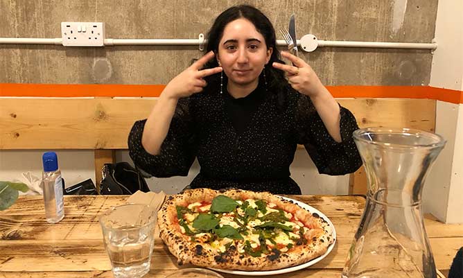 A picture of Mariam with a pizza in front of her