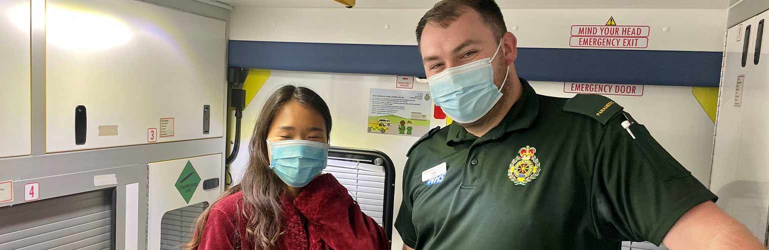 Victoria Kim with a paramedic inside an ambulance with a face covering on