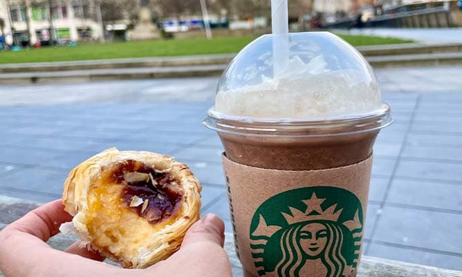 A pastry and a Starbucks coffee in the foreground and Piccadilly Gardens in the background