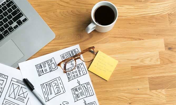 A wooden desk with a sticky pad, a cup of coffee and the corner of a laptop