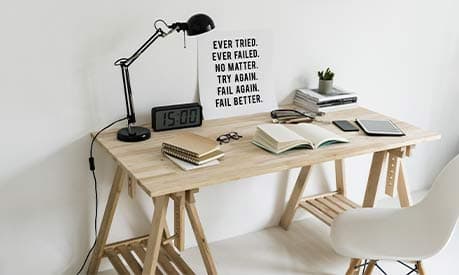 A wooden desk with a white background. On the desk is a lamp, books and a clock.