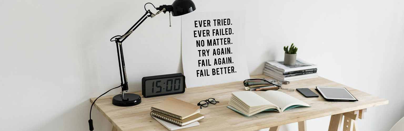 A wooden desk with a white background. On the desk is a lamp, books and a clock.