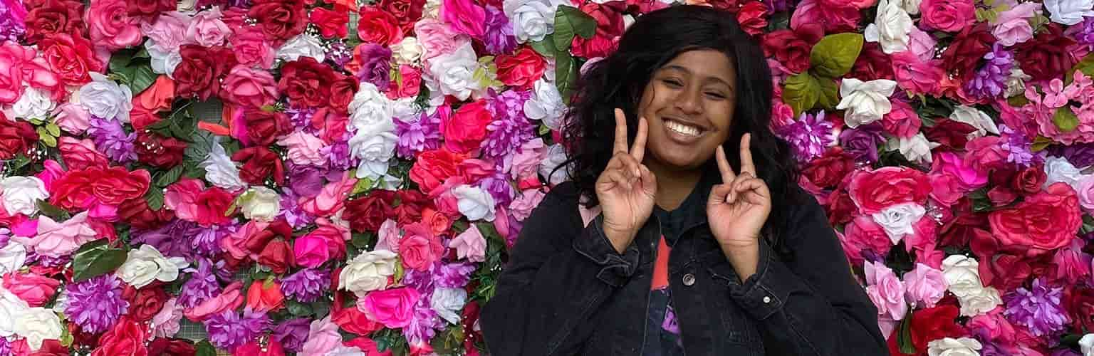 smiling woman in front of a wall of flowers