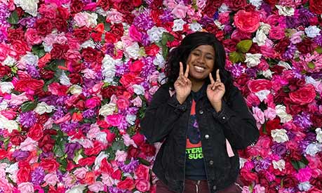 smiling woman in front of a wall of flowers