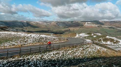 A cyclist on a tarmac road with snow on the hills in the Peak District