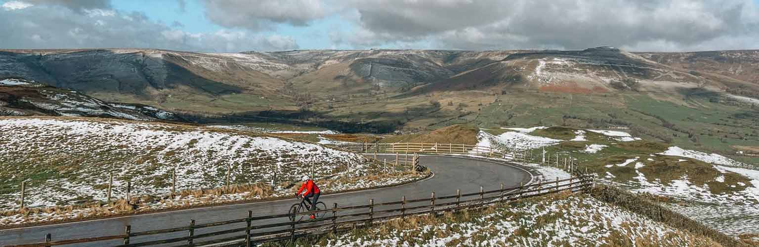 A cyclist on a tarmac road with snow on the hills in the Peak District