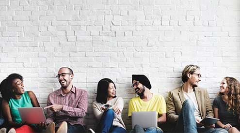 A group of people laughing sitting down leaning against a white brick wall