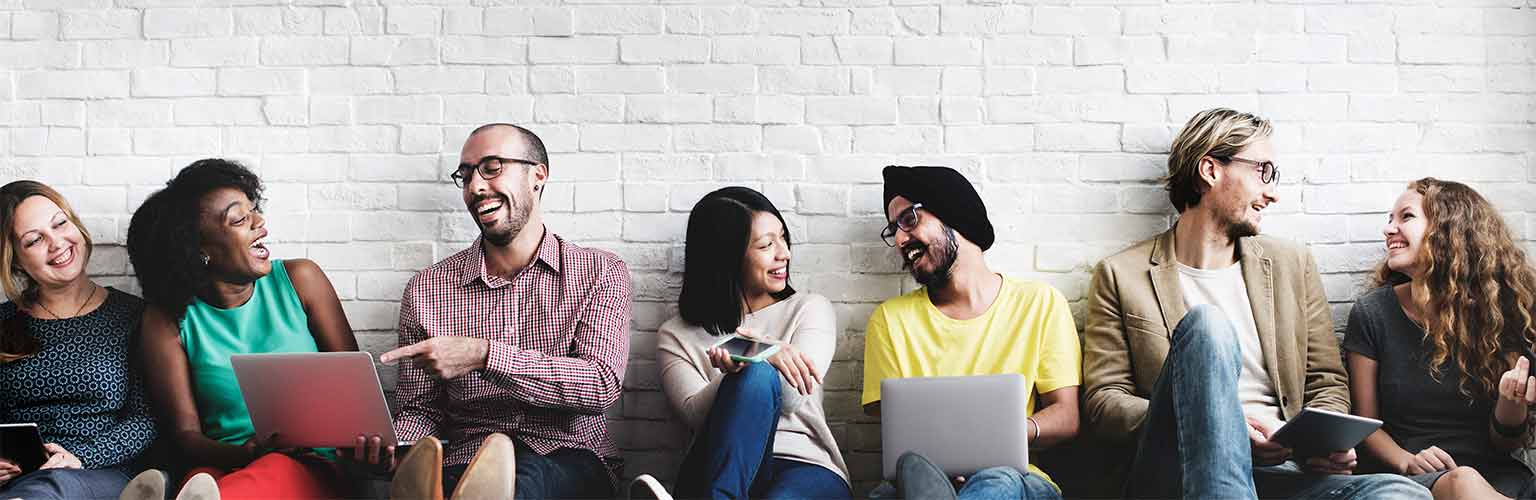 A group of people laughing sitting down leaning against a white brick wall