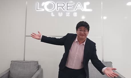 Hoi Kit Cheung standing in front of a L'Oreal sign
