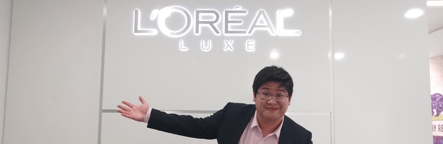 Hoi Kit Cheung standing in front of a L'Oreal sign