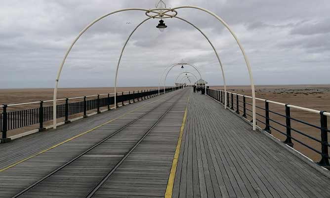 A pier on a beach during overcast conditions and low tide