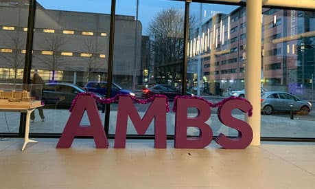 The letters 'AMBS' in purple and covered in tinsel