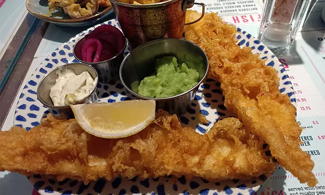A picture of the classic English food - fish and chips with a lemon on top of the fish and a side of mushy peas
