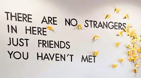 A white picture which has text in black that reads 'there are no strangers in here just friends you haven't met.' there are yellow leaves on the right hand side of the image.