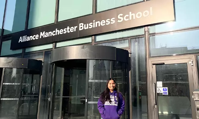 Hardika Gupta standing outside the entrance of the Alliance Manchester Business School building entrance