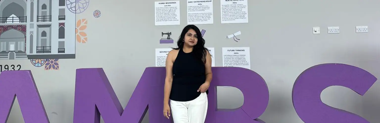 Niharika Singh, a student at Alliance Manchester Business School, standing in front of large purple letters on campus.