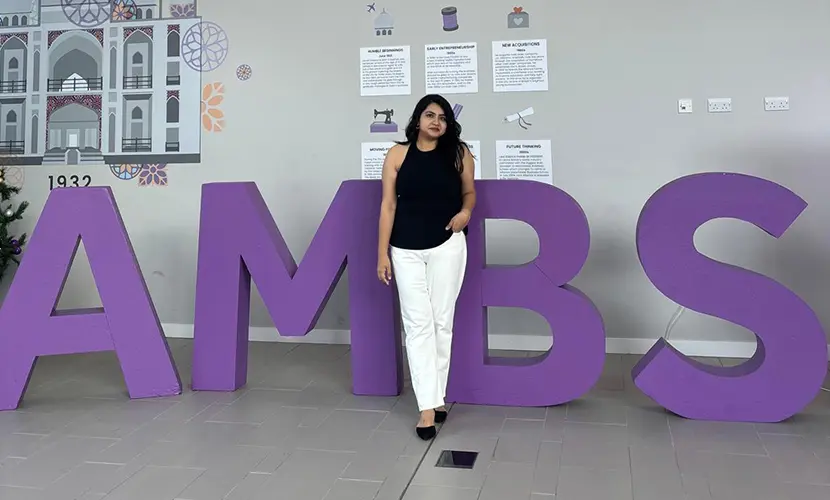 Niharika Singh, a student at Alliance Manchester Business School, standing in front of large purple letters on campus.