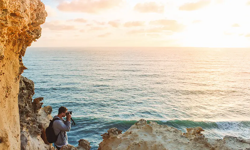 Student studying abroad taking photos on a rocky seaside cliff during sunset.
