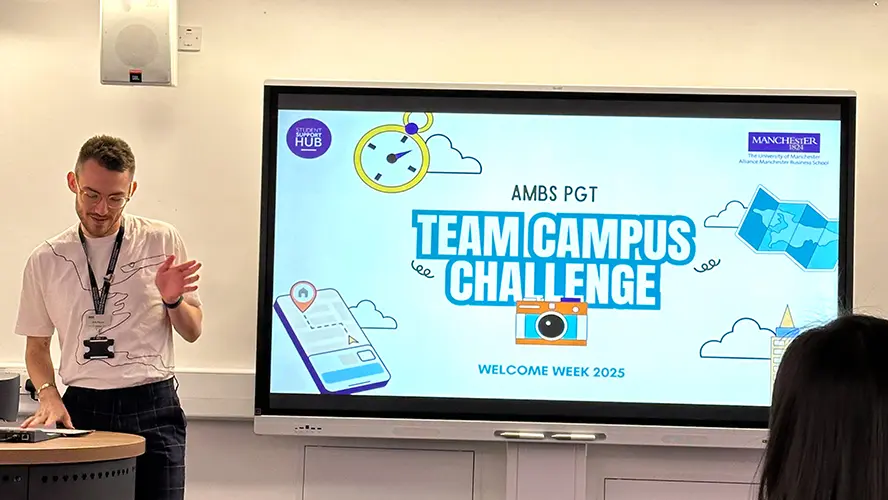 A male member of staff presenting next to a large screen that says 