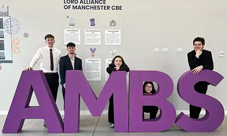 Five undergraduate students smiling for a photo between large letters that spell out AMBS.