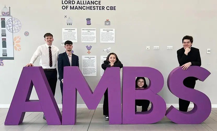 Five undergraduate students smiling for a photo between large letters that spell out AMBS.