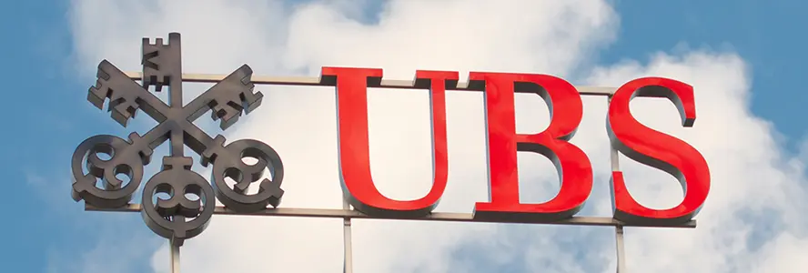 Large UBS signage featuring a red logo with a cloudy blue sky in the background.