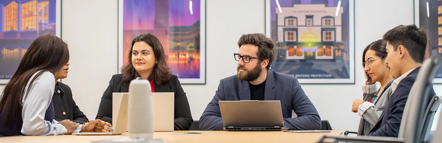 Six MBA students working on laptops in a boardroom.
