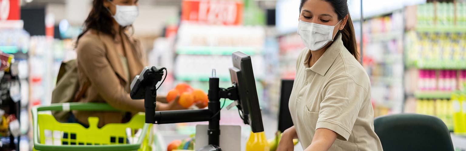 supermarket employee scanning items wearing a face covering