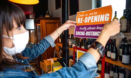 shop worker wearing face covering hanging a reopening sign