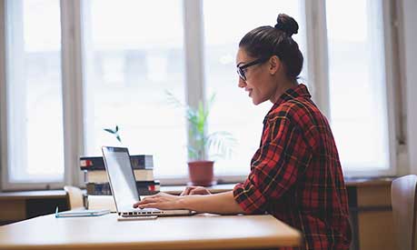 A student sitting at a desk and looking at a laptop