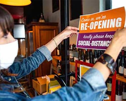 A woman putting up a sign in a shop saying reopening