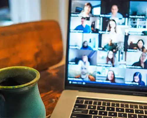 A screen showing webinar attendees on a laptop. In the foreground is a cup of coffee.
