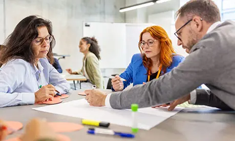 Three professionals in a classroom environment working together around a table on a project