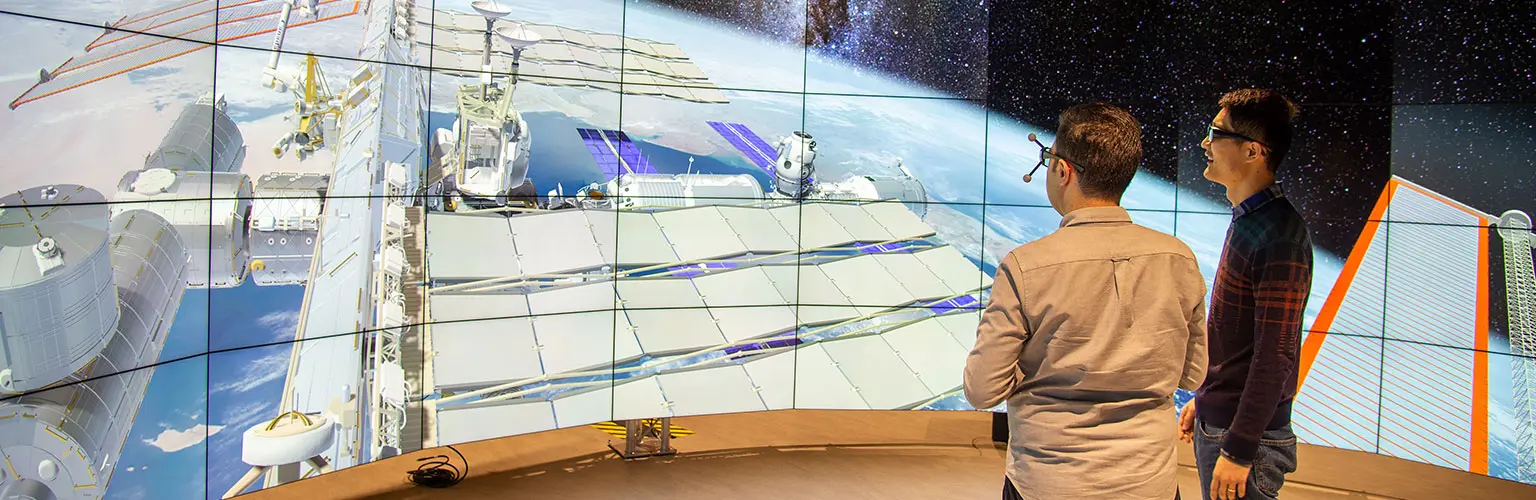 Two professional men wearing 3D glasses stood in front of a wide angle 3D screen looking at a data visualisation of space
