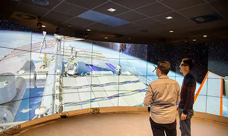 Two professional men wearing 3D glasses stood in front of a wide angle 3D screen looking at a data visualisation of space