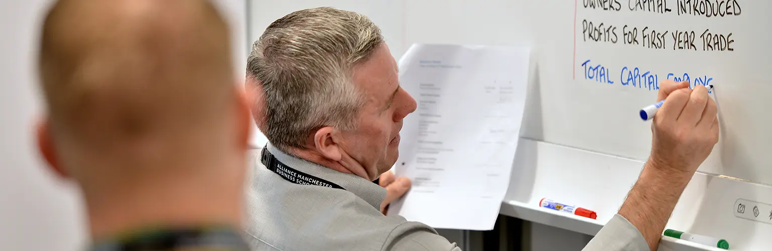 Two professionals writing down notes on a whiteboard in a classroom setting